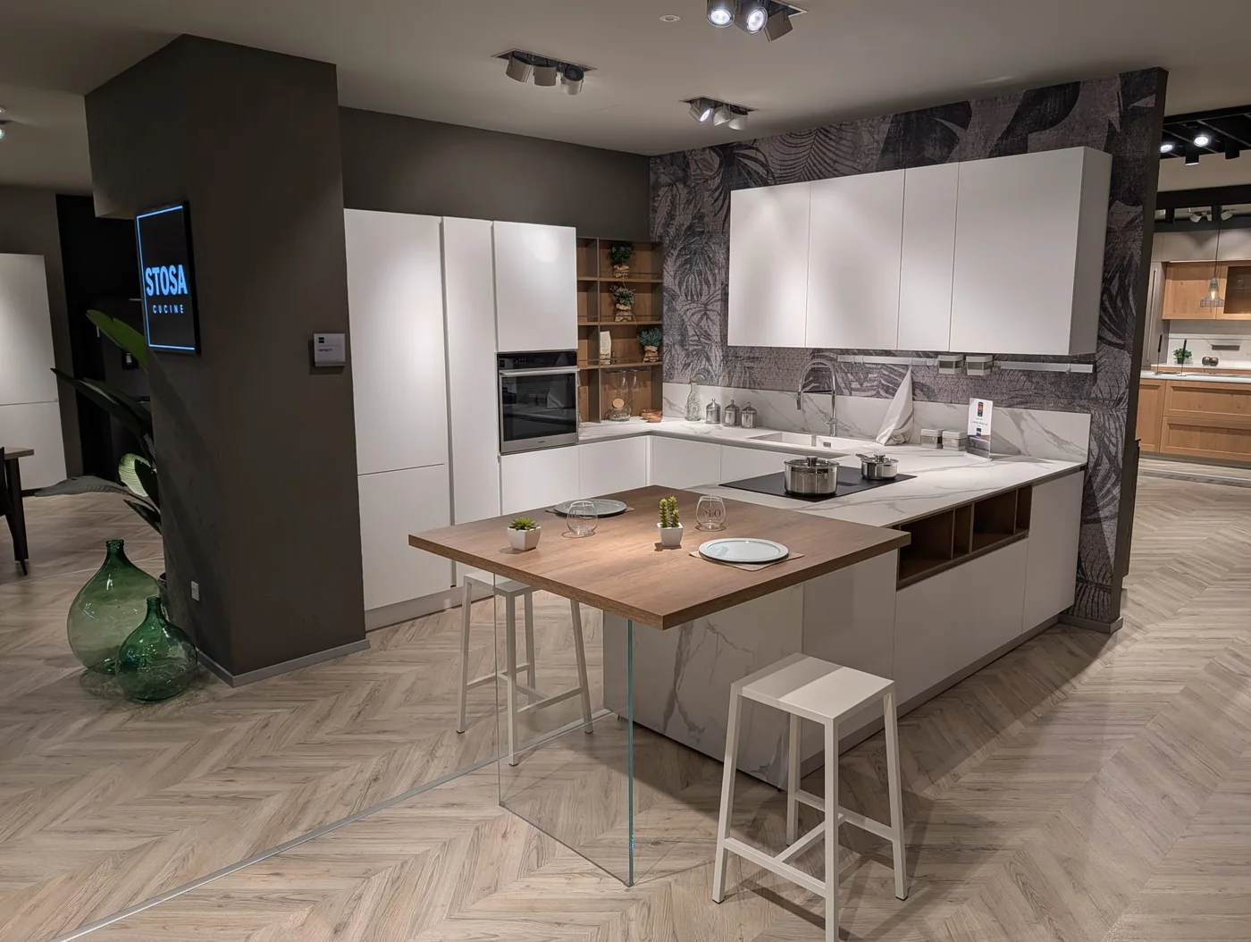 Cucina Stosa Infinity in PET bianco opaco con penisola snack e particolari in rovere nodato, top HPL calacatta, nello showroom di Veduggio